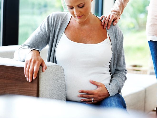 pregnant woman looking at bump with comforting hand