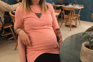 A photo of Agota with a baby bump, sitting down in a cafe. 