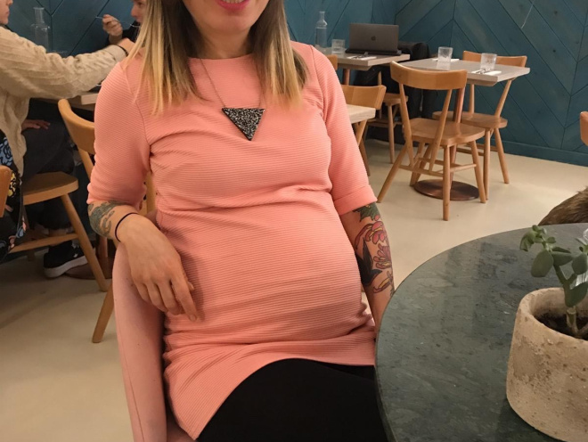 A photo of Agota with a baby bump, sitting down in a cafe. 