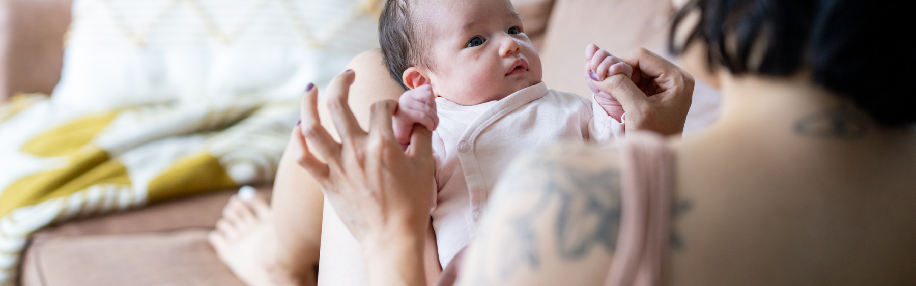Mother or birthing person holding baby on her knee on sofa