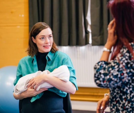 Antenatal class - woman holding a baby doll talking to a course leader