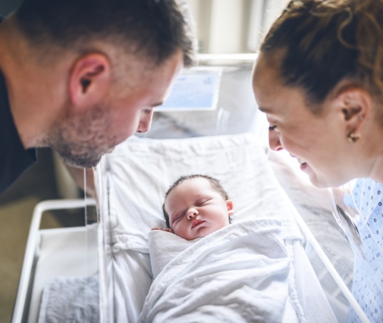 Newborn baby in hospital with parents looking over