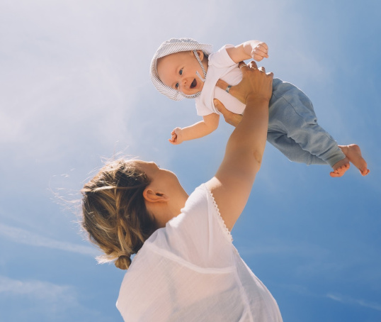 Mum holding her baby up in front of a clear sky