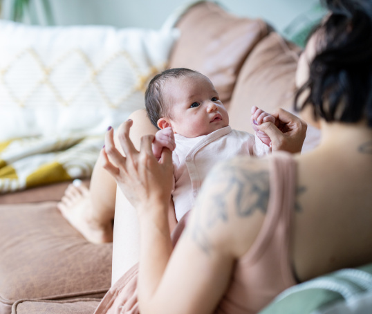 Mother or birthing person holding baby on her knee on sofa