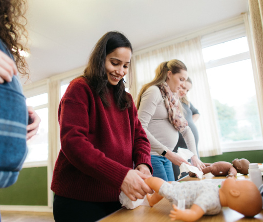 Pregnant woman smiling and changing nappy on a doll at an antenatal class