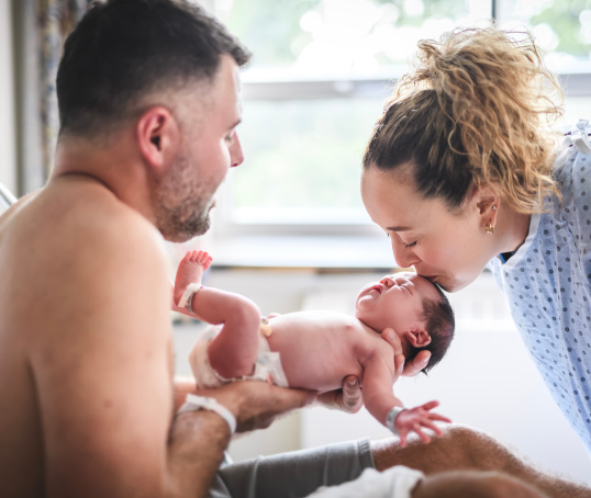 Dad holding newborn baby and mum kissing baby on head