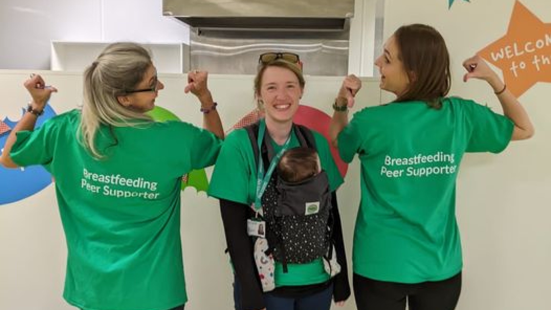 Two breastfeeding peer supporters with a mother carrying a baby in a sling