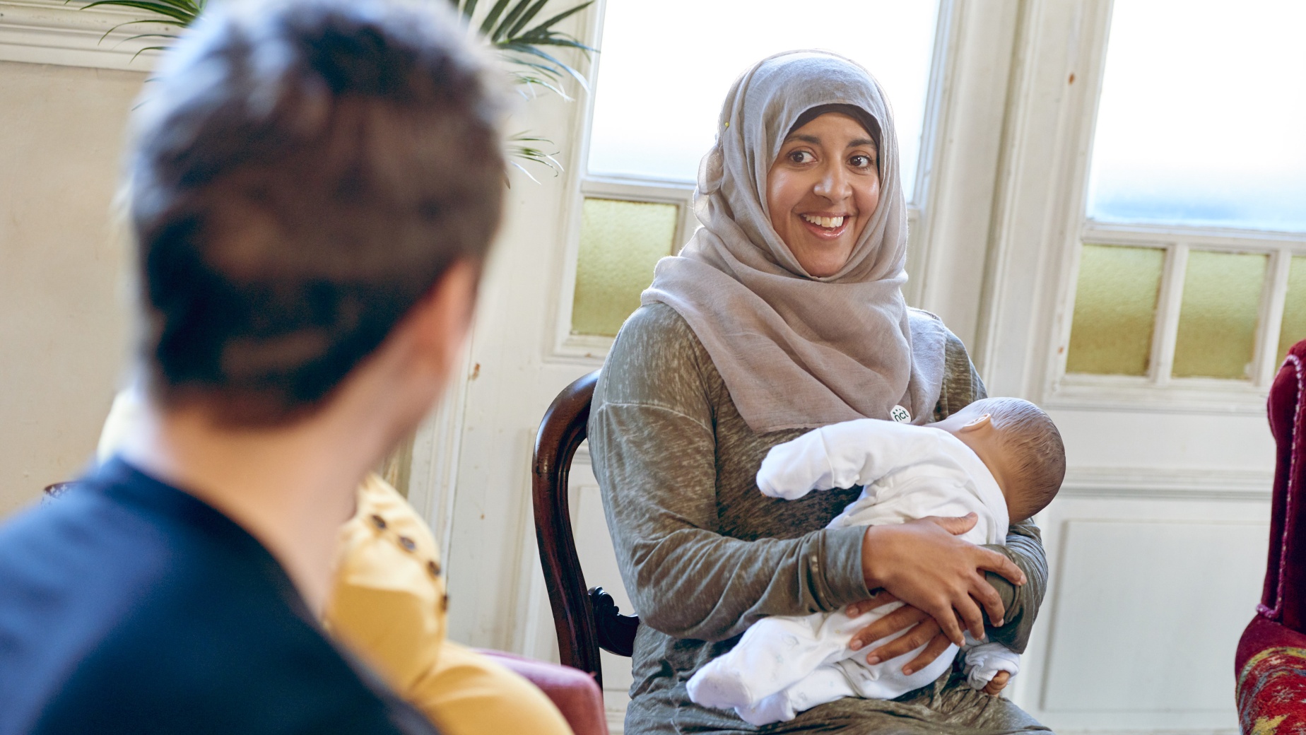 Woman holding baby and sitting down at a postnatal group