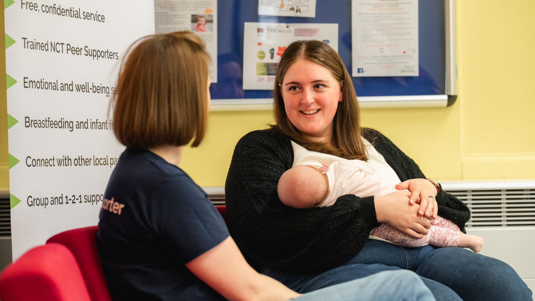 Mum holding her baby talking to a peer supporter