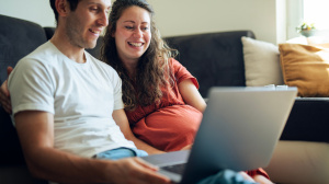 Pregnant couple sitting on a sofa looking at a laptop