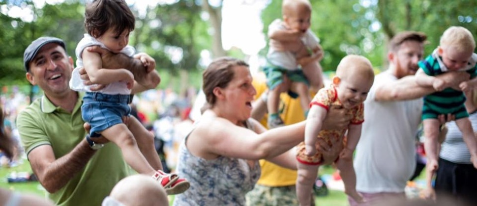 Parents in park setting swinging babies into centre of circle