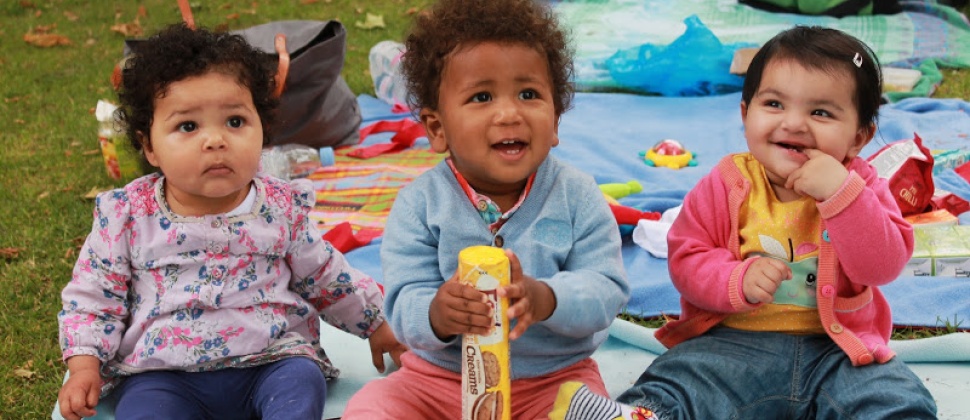 Three older babies sitting on a picnic blanket looking cute and cheeky in Newham
