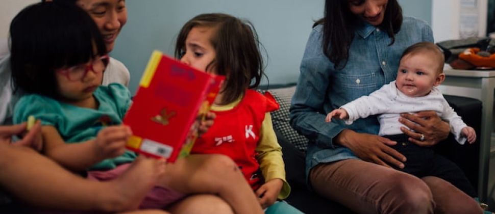 Two mums reading to their children