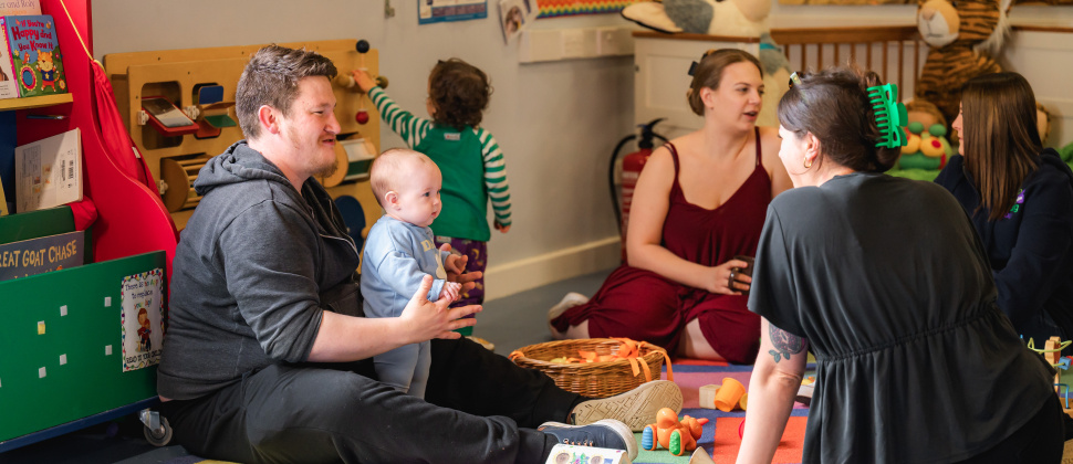 Parents and children sat on the floor inside a hall at an NCT playgroup