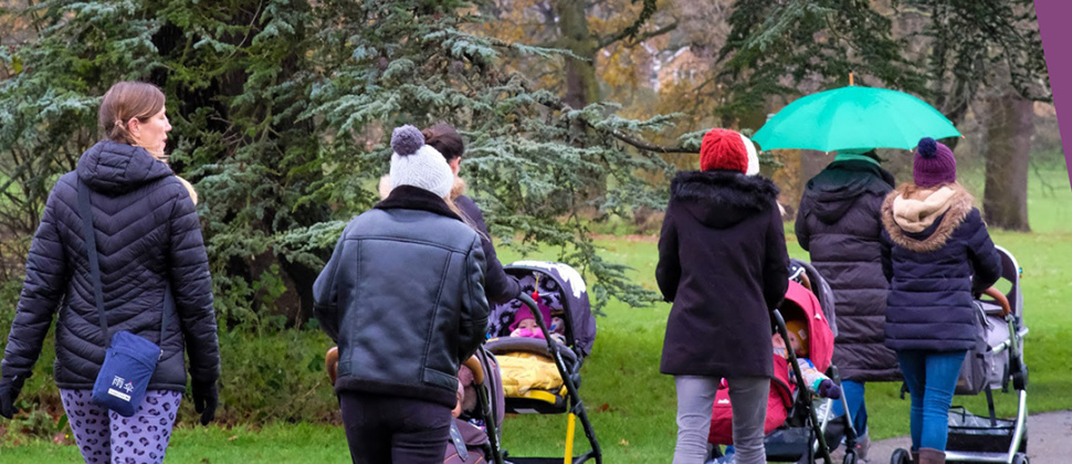 Adults with pushchairs walking in the rain with wording NCT Walk and Talk above
